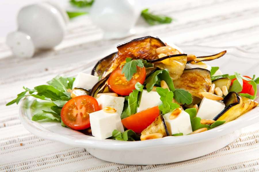Grilled eggplant tomato feta salad with pine nuts and arugula in a white bowl. — Salad Background