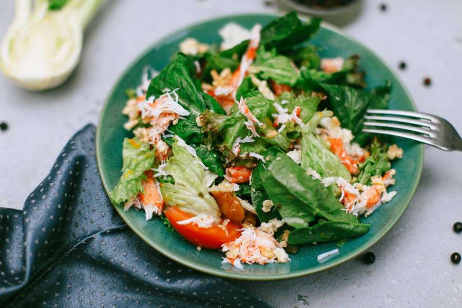 Uma salada fresca de caranguejo com verduras e tomate em um prato azul-petróleo com um garfo. — Salada Papéis de Parede