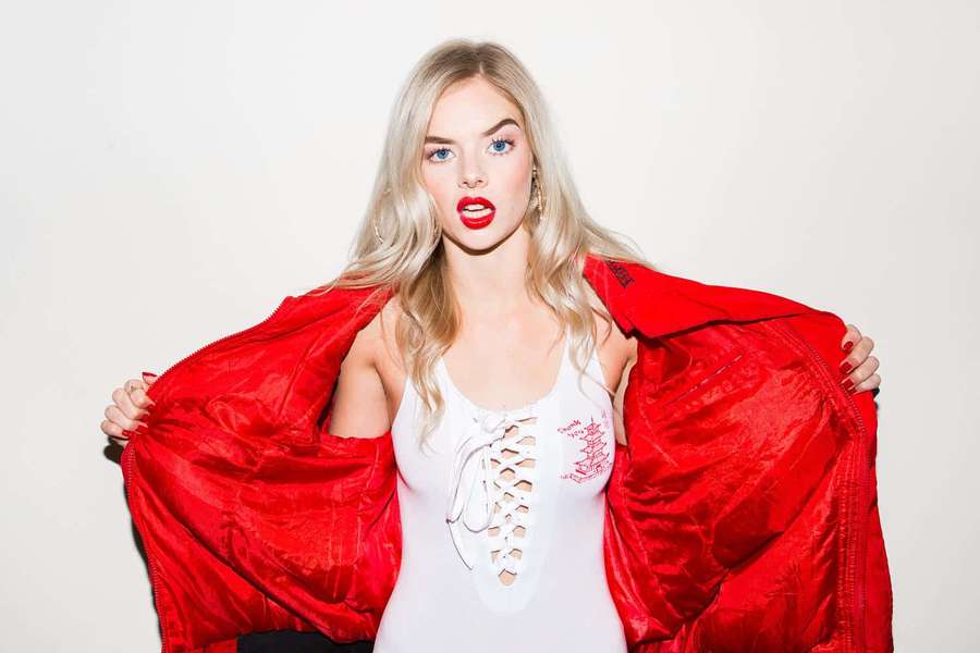 Blonde woman in white top holding open red jacket with red lips. — Samara weaving Wallpaper
