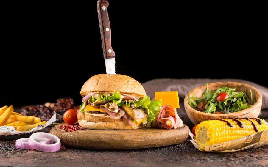 Hambúrguer gourmet com batatas fritas, salada e milho em uma tábua de madeira contra fundo preto — Sanduíche Papéis de Parede