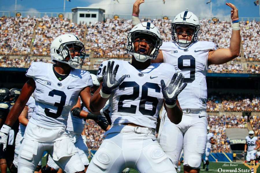 Football players in white uniforms celebrate on a sunny field with fans in the stands. — Saquon Barkley Wallpaper