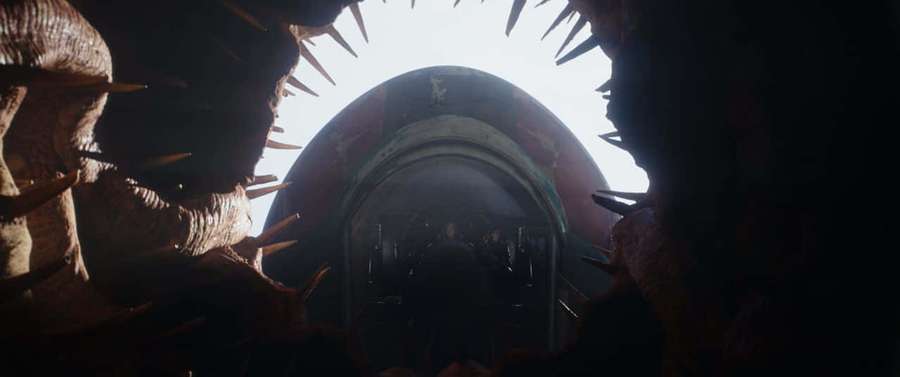 A dark tunnel with jagged spikes frames a bright circular opening revealing a distant figure in shadow. — Sarnia Wallpaper