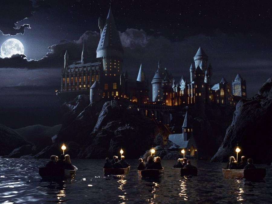 Studenten in Ruderbooten mit Laternen nähern sich einem Schloss in einer mondhellen Nacht. — Schloss Hogwarts Wallpaper