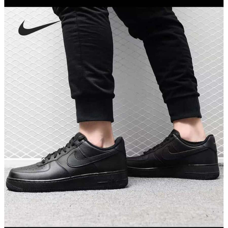 Schwarze Nike Air Force 1 Sneaker mit schwarzen Jogginghosen auf grauem Teppich. — Schwarze Luftwaffe Bild Wallpaper