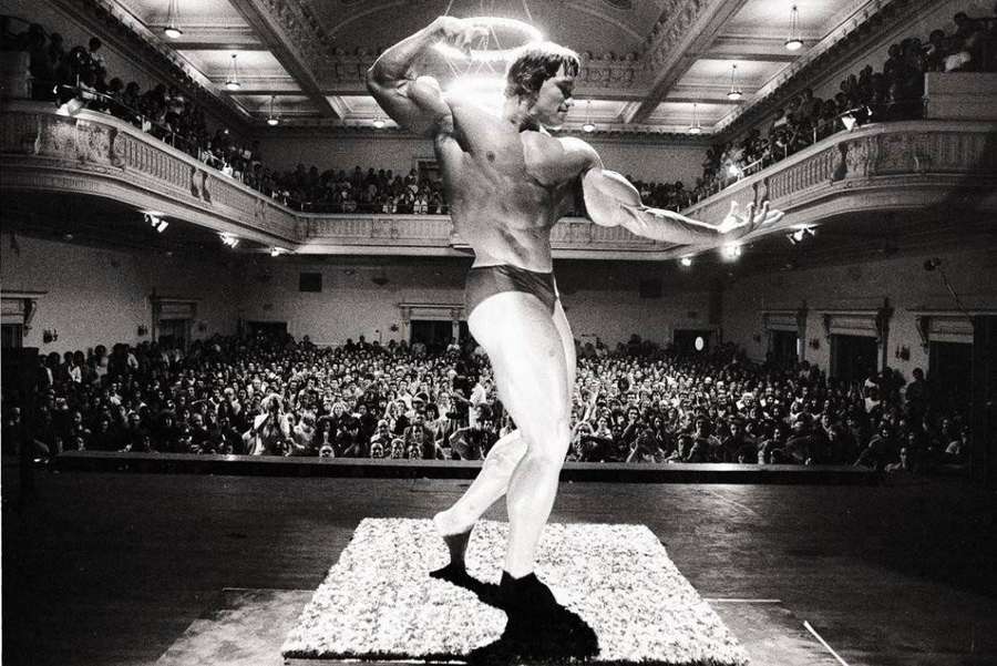 Bodybuilder posing on stage during a competition in a crowded theater. — Schwarzenegger Wallpaper