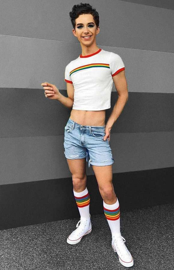 Person in Regenbogen-Outfit lächelt vor grauer Wand — Schwuler Junge Wallpaper