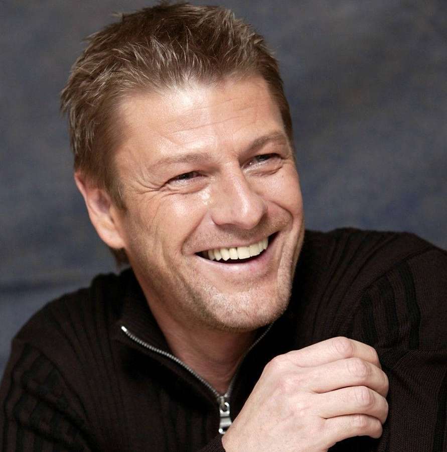 A smiling man in a black sweater posing for a studio portrait. — Sean Bean Wallpaper