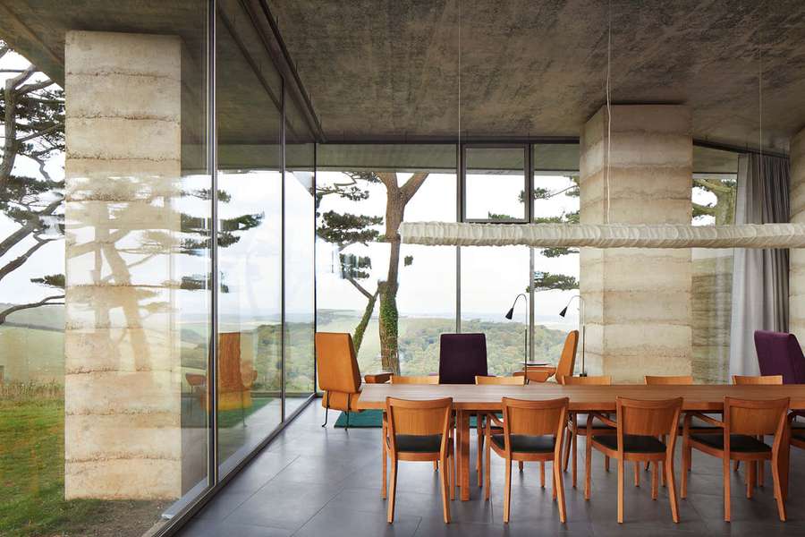 Ruang makan modern dengan kursi kayu dan pilar beton menghadap pemandangan hijau. — Sekuler Wallpaper