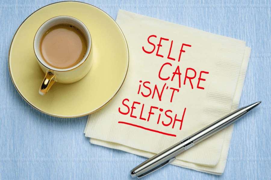 Yellow coffee cup next to napkin with red self care message and pen. — Self Care Wallpaper