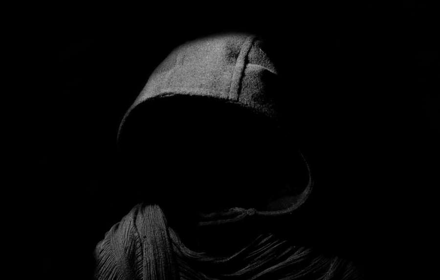 A person in a dark hooded garment with face obscured by shadow. — Shadow Background
