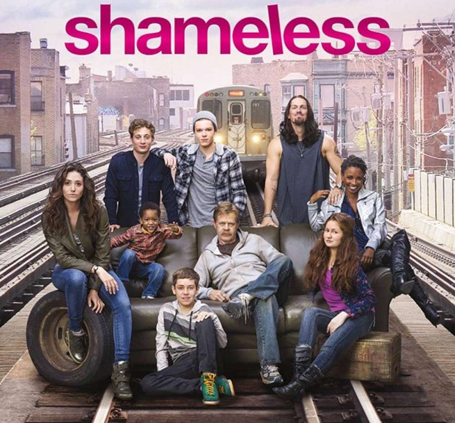 A TV show cast sits on a couch on subway tracks with a train approaching. — Shameless Background