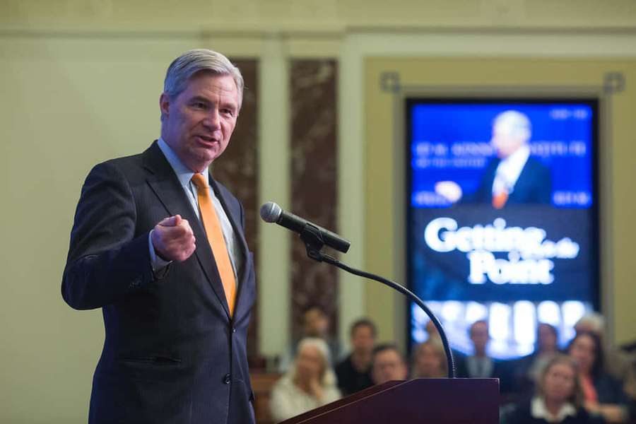 Man in suit giving speech at podium with audience and screen behind him. — Sheldon Whitehouse Wallpaper
