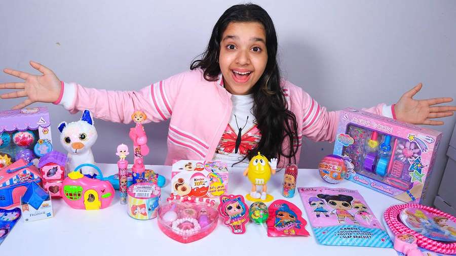 Excited girl surrounded by colorful toys and dolls on a white table. — Shfa Wallpaper