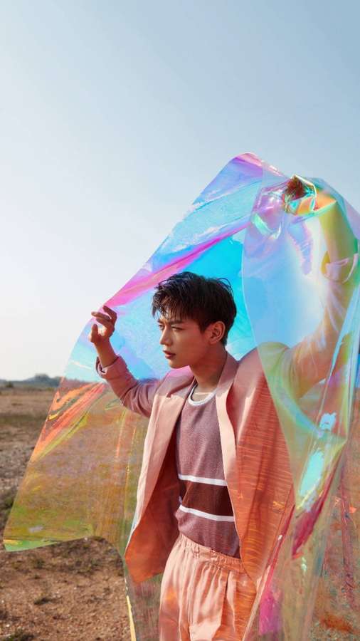 Junger Mann hält schillernden Regenbogenstoff auf trockenem Feld unter blauem Himmel — Shinee Bilder