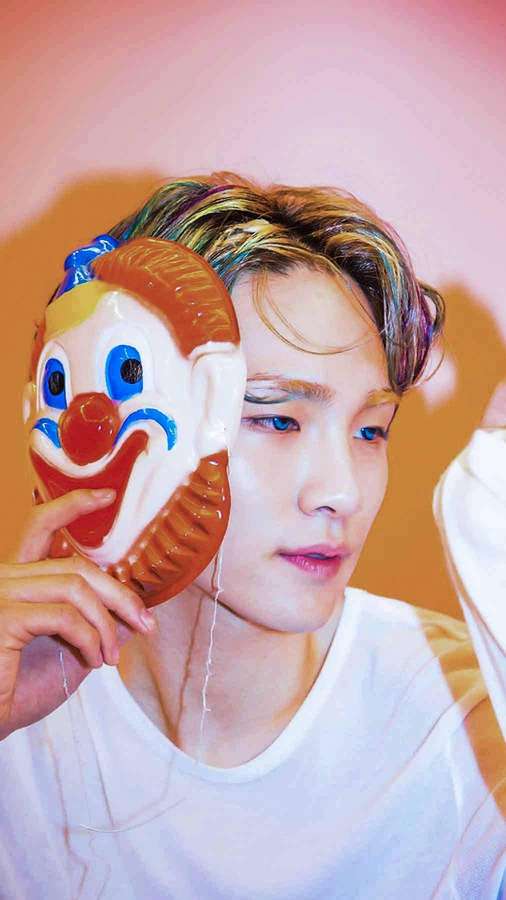 Junger Mann mit Regenbogenhaaren hält eine Clownmaske in einem Studio mit rosa und orangener Beleuchtung. — Shinee Hintergrundbild