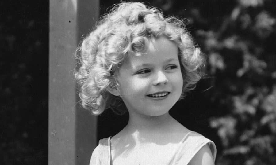 Ein junges Mädchen mit lockigem Haar lächelt sanft draußen in einem Vintage-Schwarzweißfoto. — Shirley Bilder