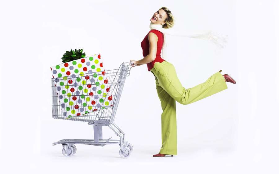 Woman pushing shopping cart with gift smiling and kicking leg up. — Shopping Background