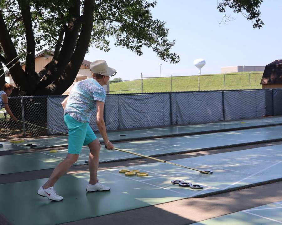 Person spielt Curling auf einem sonnigen Außenplatz mit Bäumen und Zaun im Hintergrund. — Shuffleboard Bilder