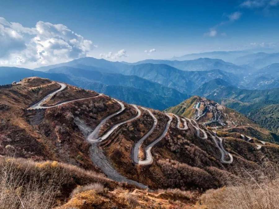 Kurvenreiche Bergstraße durch herbstliche Hügel unter blauem Himmel mit Wolken. — Silk Road Bilder