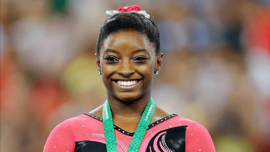 Gymnast smiling proudly with medal around neck in competition attire. — Simone Biles Wallpaper