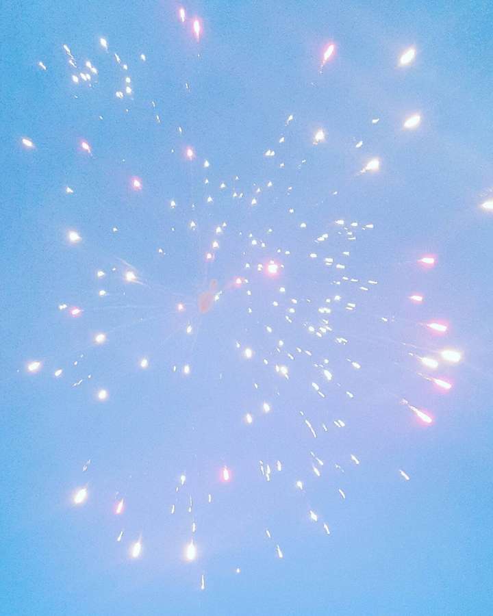 Fireworks bursting in a clear blue sky with pink and white sparks. — Simple Blue Aesthetic Background
