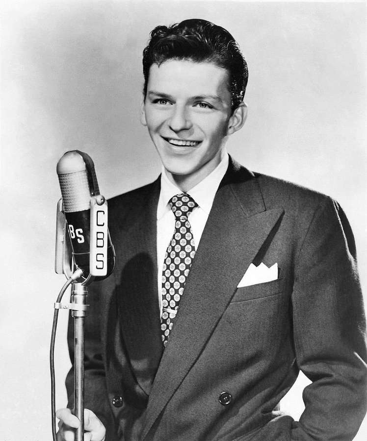 A smiling man in a suit holding a vintage CBS microphone. — Sinatra Background