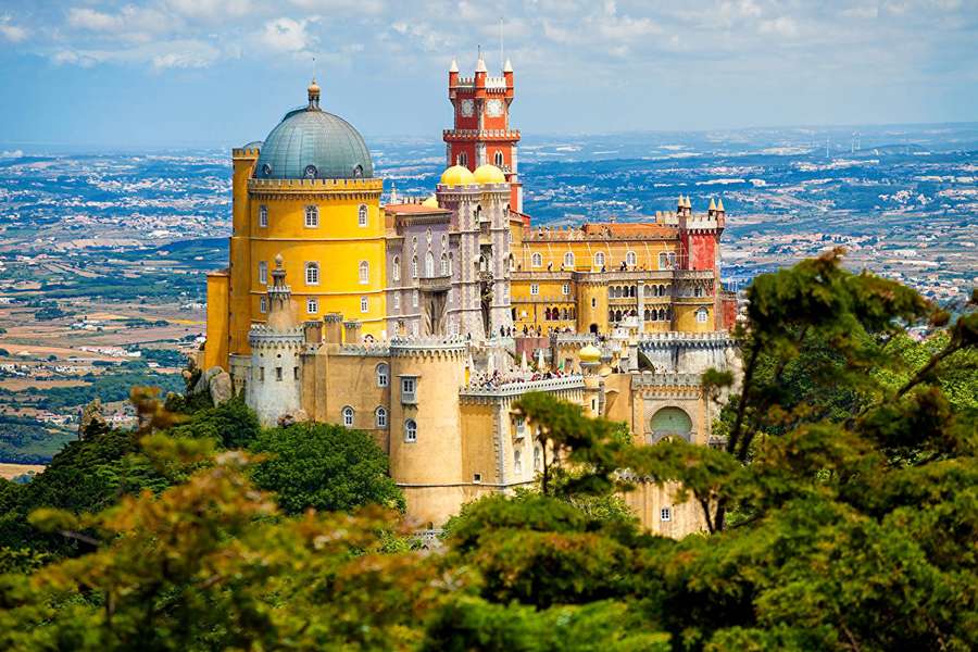 Un castello colorato su una collina con alberi verdi e una valle sottostante. — Sintra Sfondi