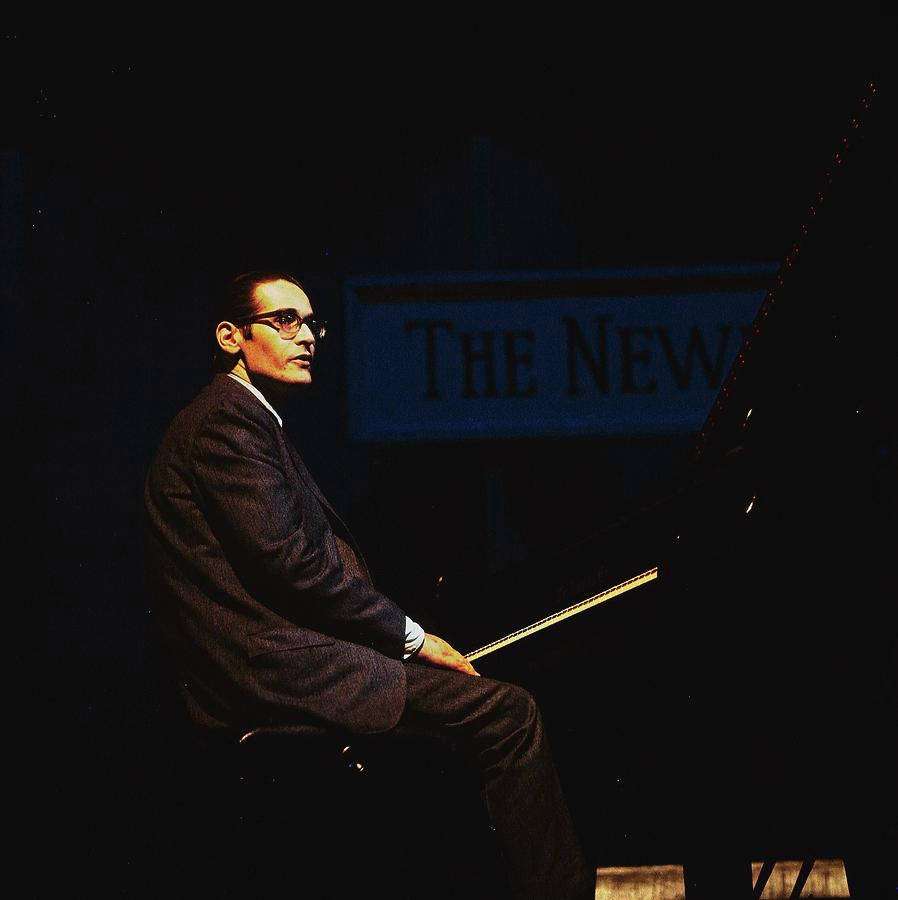 Man in suit and glasses seated at piano on stage under spotlight. — Sit down Wallpaper