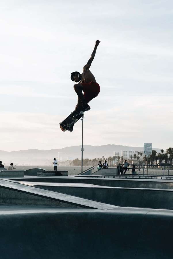 Skateboarder utfører lufttriks i urban skatepark nær havet — Skater Bakgrunner