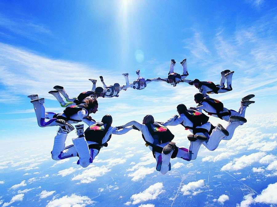 Skydivers holding hands in a circle above clouds under bright sun. — Skydiving Picture