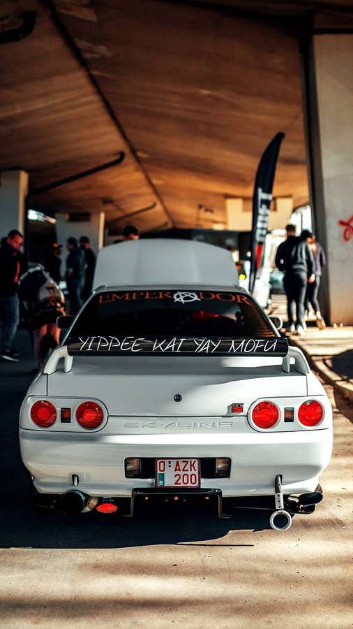 White Nissan Skyline R32 with red taillights at a car meet under wooden canopy. — Skyline R32 Wallpaper