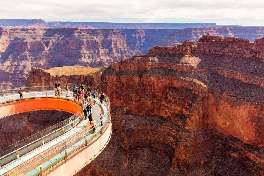 People walking on a curved glass skywalk overlooking the Grand Canyon's red rock cliffs. — Skywalker Background