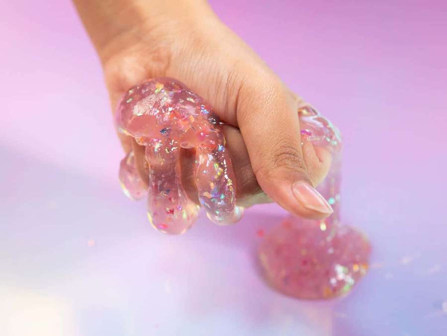 Hand molding sparkly pink slime on a gradient purple surface. — Slime Background