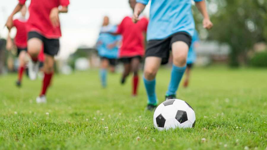 Young soccer players in red and blue jerseys running on a grass field with a soccer ball in focus. — Soccer Background