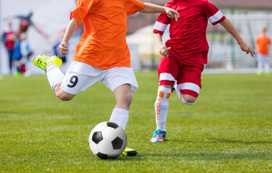 Unge fodboldspillere i orange og røde uniformer kæmper om en bold på en græsbane. — Soccer Ball Wallpapers