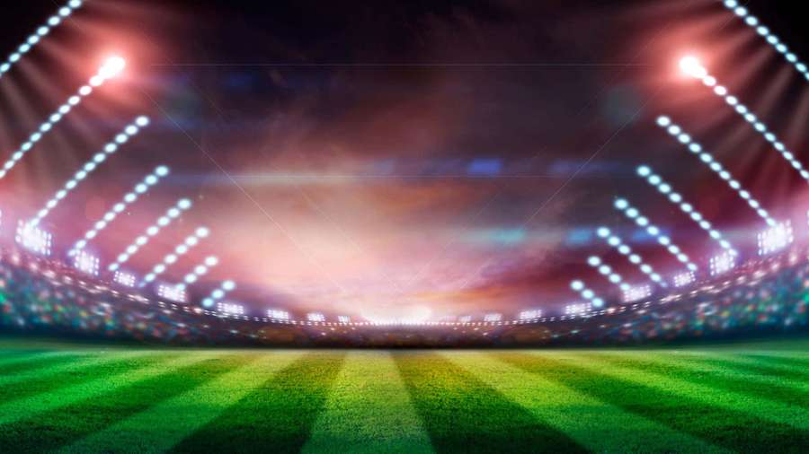 A brightly lit empty sports stadium at night with green grass and colorful sky. — Soccer Stadium Background