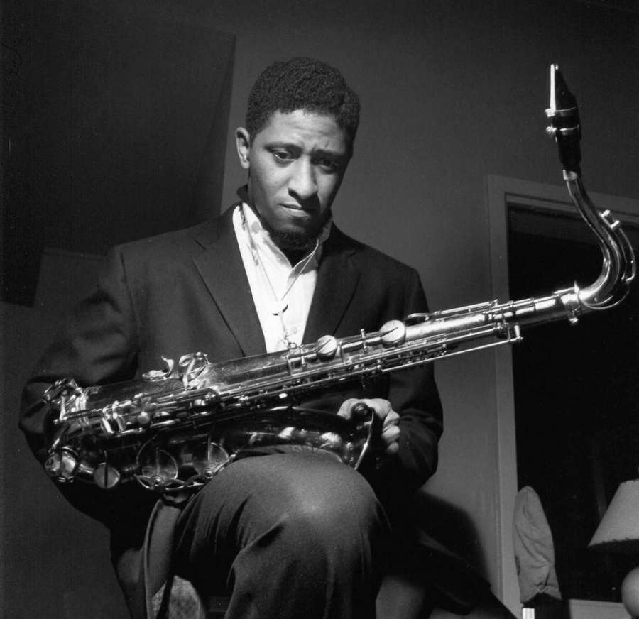 A man in a suit holding a saxophone in a dimly lit studio. — Sonny Rollins Wallpaper