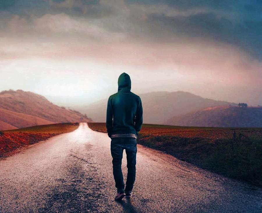 Pessoa de moletom caminhando por uma longa estrada em direção a montanhas ao entardecer. — Sozinho Papéis de Parede