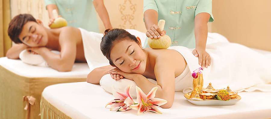 Two people receiving Thai stone massages in a spa with pink lilies and offerings. — Spa Picture