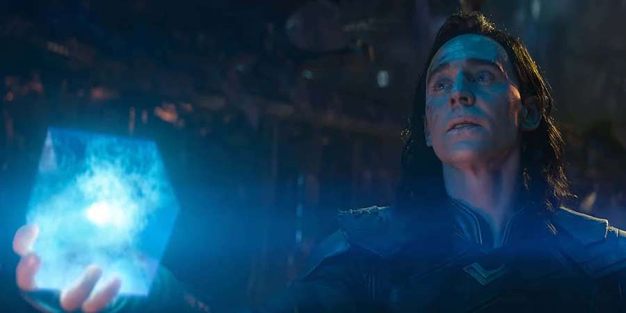 Loki holding a glowing blue cube in a dark mystical setting. — Space Stone Wallpaper