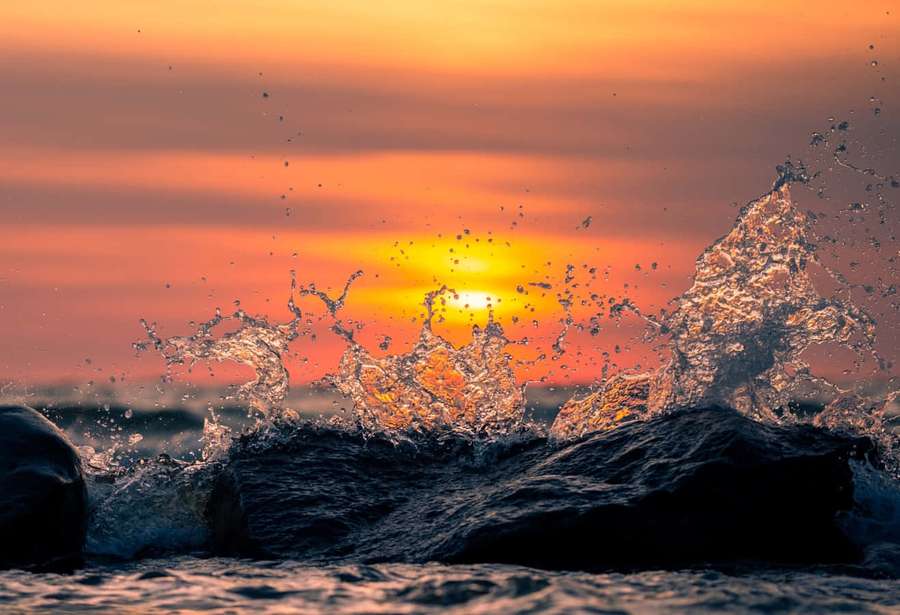 Ocean waves crash against rocks at sunset with vibrant orange and gold lighting. — Splash Picture