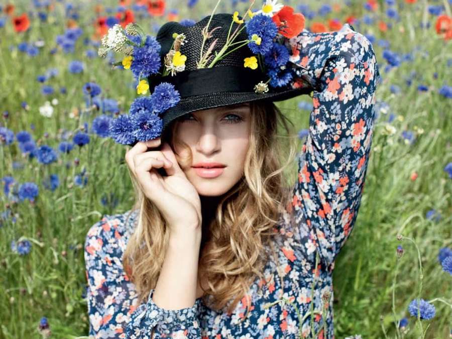 Woman in floral dress and flower-adorned hat standing in a field of wildflowers. — Spring Fashion Wallpaper