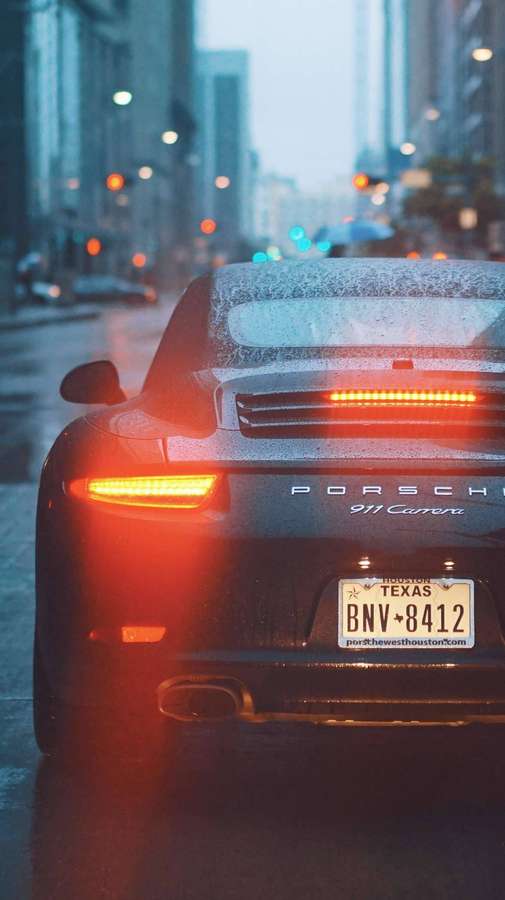 Schwarzer Porsche 911 Carrera mit roten Rücklichtern auf regnerischer Stadtstraße in der Dämmerung. — Stadt Rain Wallpaper