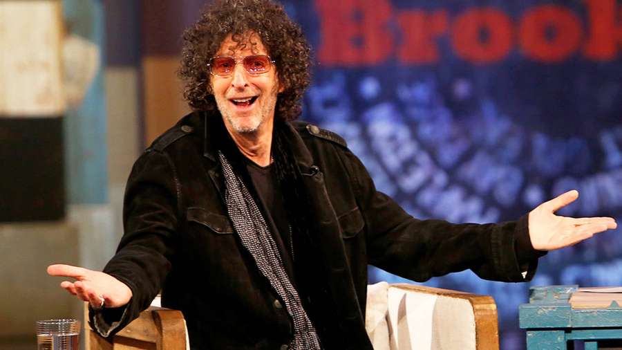 Man met krullend haar en zonnebril lachend op een talkshow-set. — Stern Achtergronden