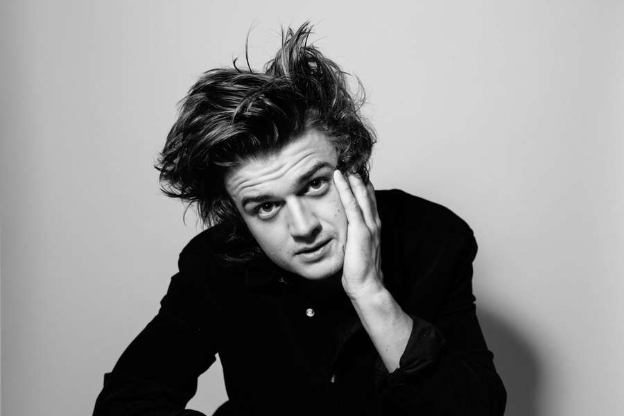 Young man with messy hair resting his hand on his cheek in a studio portrait. — Steve Harrington Background