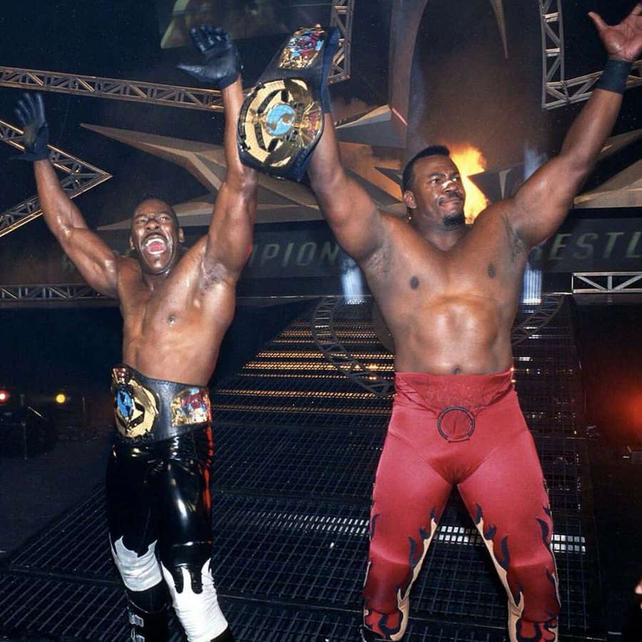 Two wrestlers holding championship belts in victory pose on stage. — Stevie Ray Wallpaper