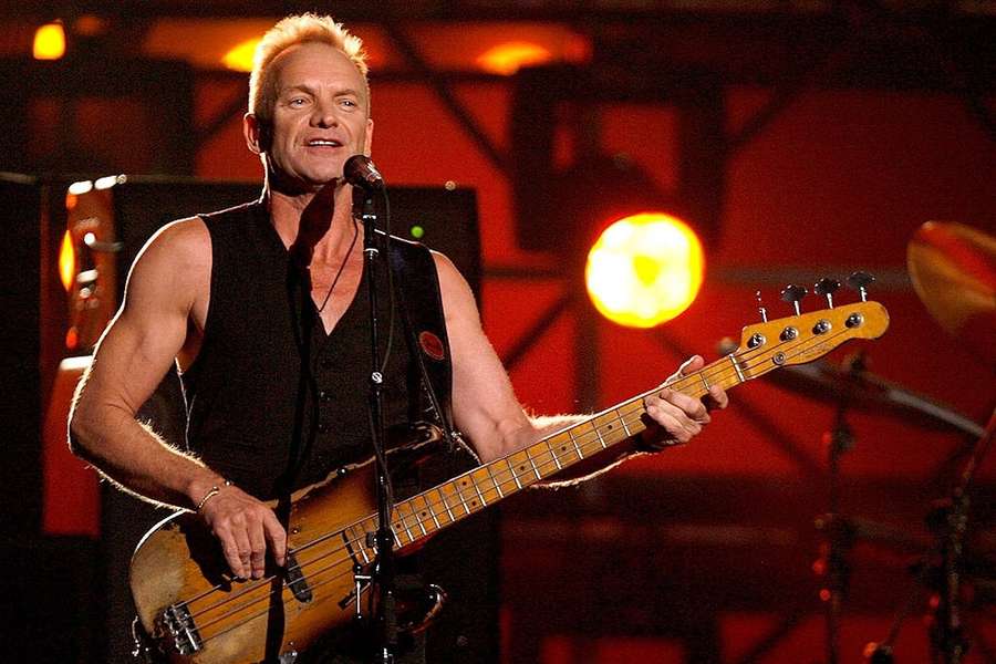 Ein männlicher Musiker, der auf der Bühne unter warmen Bühnenlichtern Bassgitarre spielt. — Sting Bilder