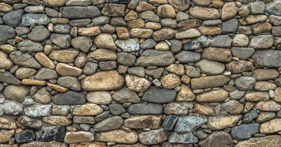 Rustic stone wall with varied earthy tones and rough textures. — Stone Wall Background
