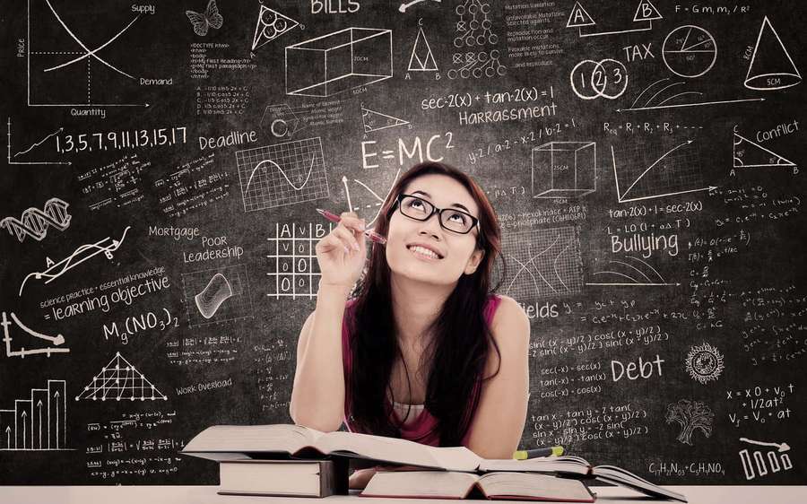 Young woman studying with books and chalkboard full of equations and diagrams. — Studious Wallpaper