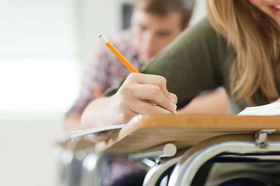 Student writing with pencil at wooden desk in classroom — Studious Picture